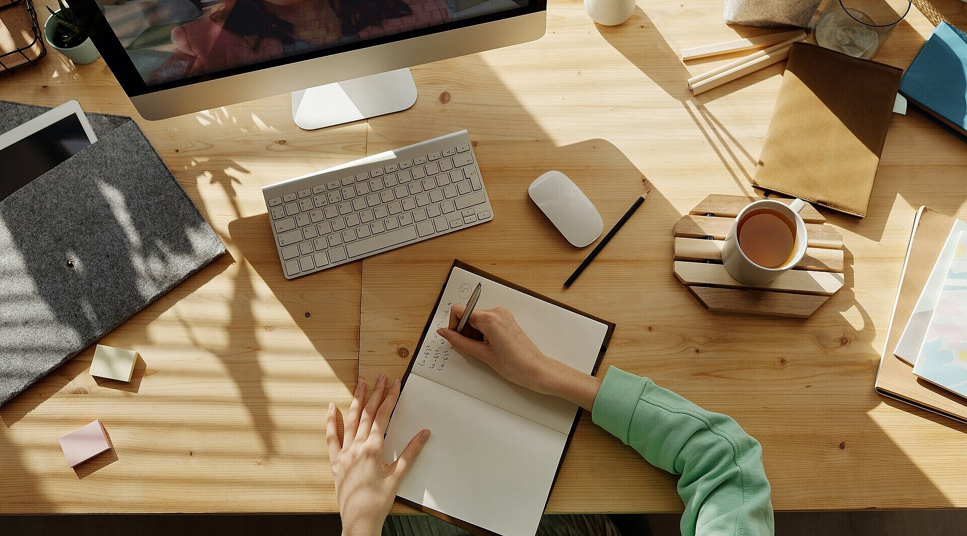 Person sitzt an Schreibtisch und schreibt in ein Heft