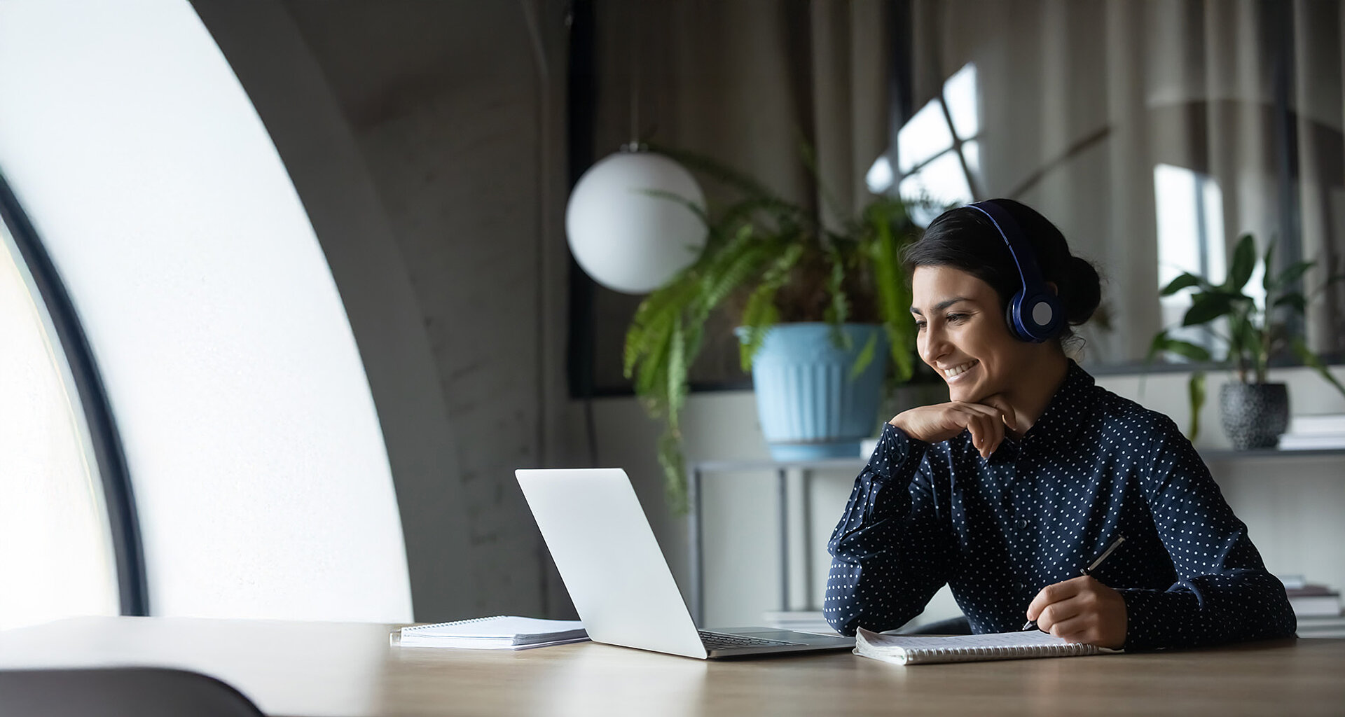 Lächelnde Dame sitzt an einem Tisch mit Laptop und Headset